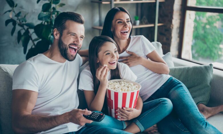 Familie lacht beim Filmabend auf dem Sofa mit Popcorn