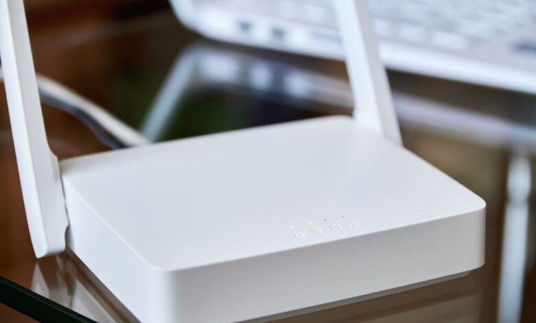 Weißer WLAN-Router auf einem Glastisch vor einem Laptop.